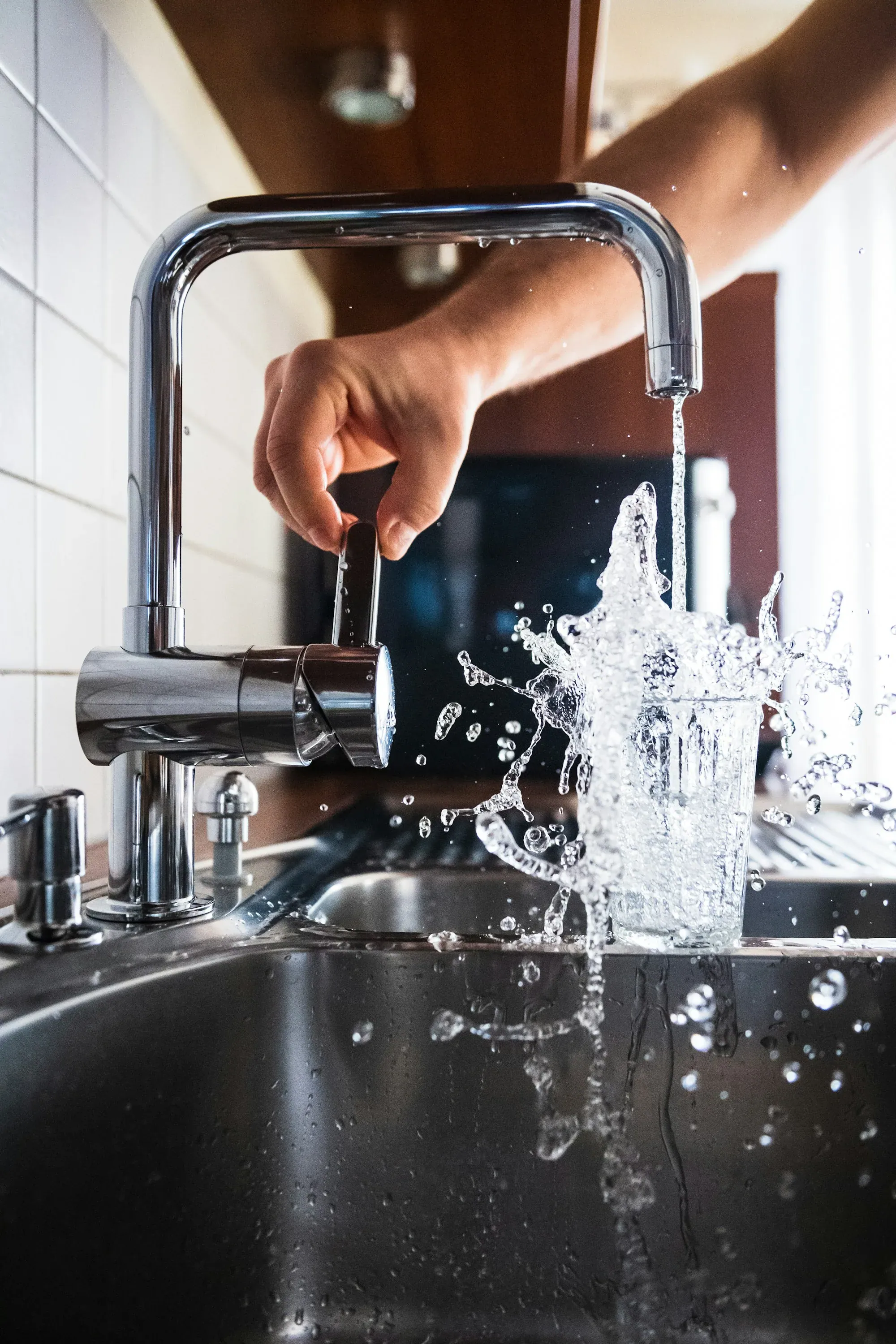 Clear drinking water filling a glass at a bright kitchen sink